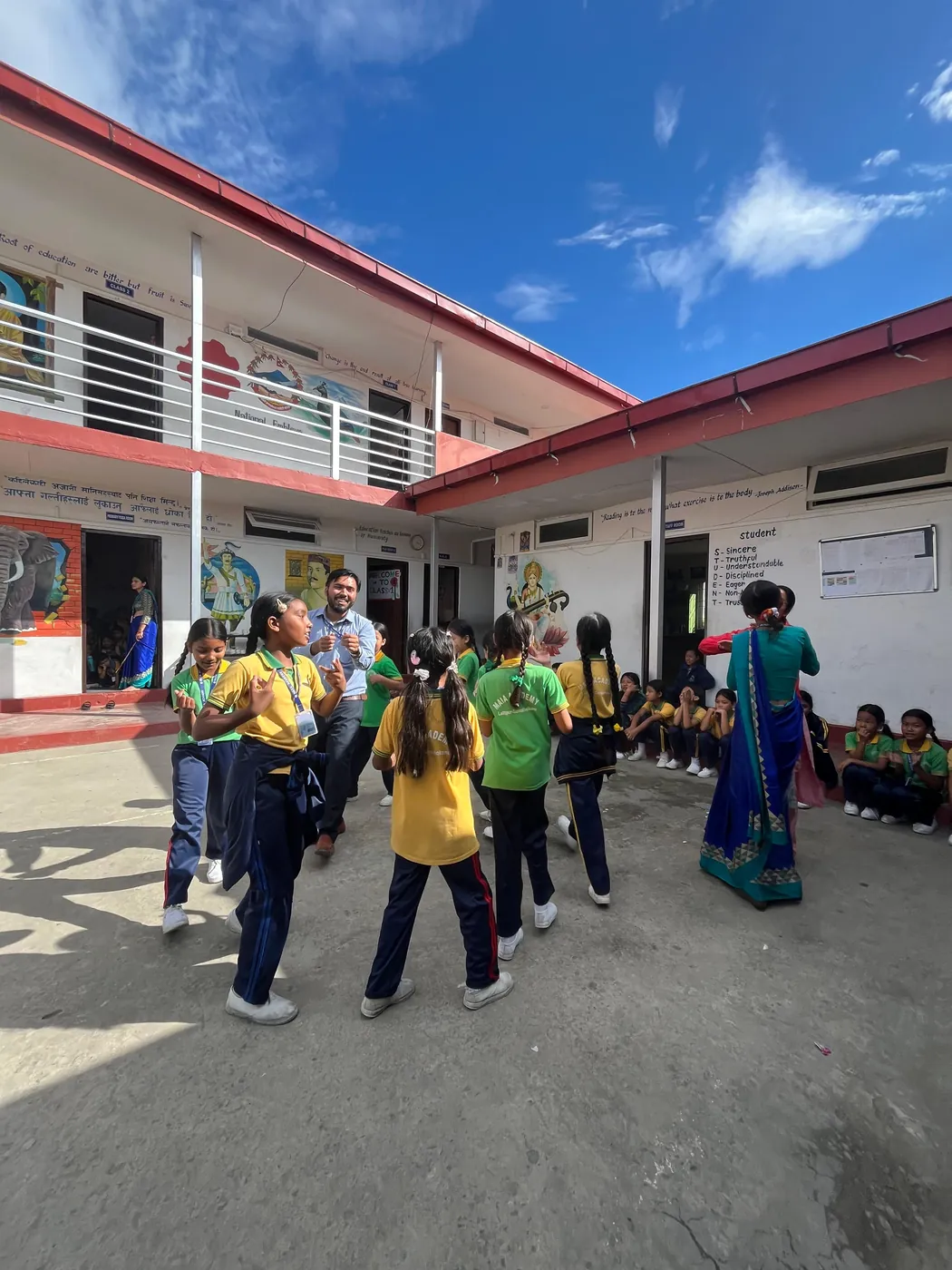 Maia Academy students practicing dance with teachers in the school courtyard under a blue sky